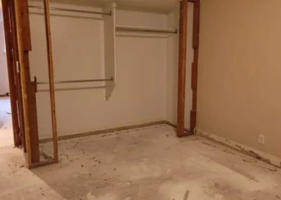 An empty room under renovation, with a partially demolished closet frame and exposed wooden studs, and a concrete or subfloor.