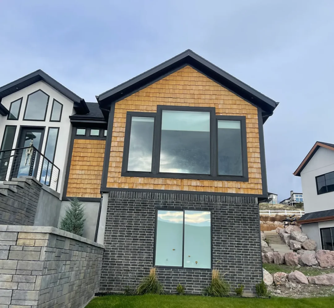 The front exterior of a modern multi-story house with dark grey brick on the first floor and horizontal wood paneling on the second, featuring large black-framed windows and a distinct roofline. The front exterior of a modern multi-story house with dark grey brick on the first floor and horizontal wood paneling on the second, featuring large black-framed windows and a distinct roofline.