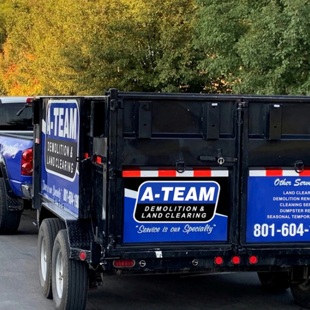 dumpster truck A close-up of an A-Team Demolition & Land Clearing trailer parked outdoors, featuring a blue and black logo with contact info.